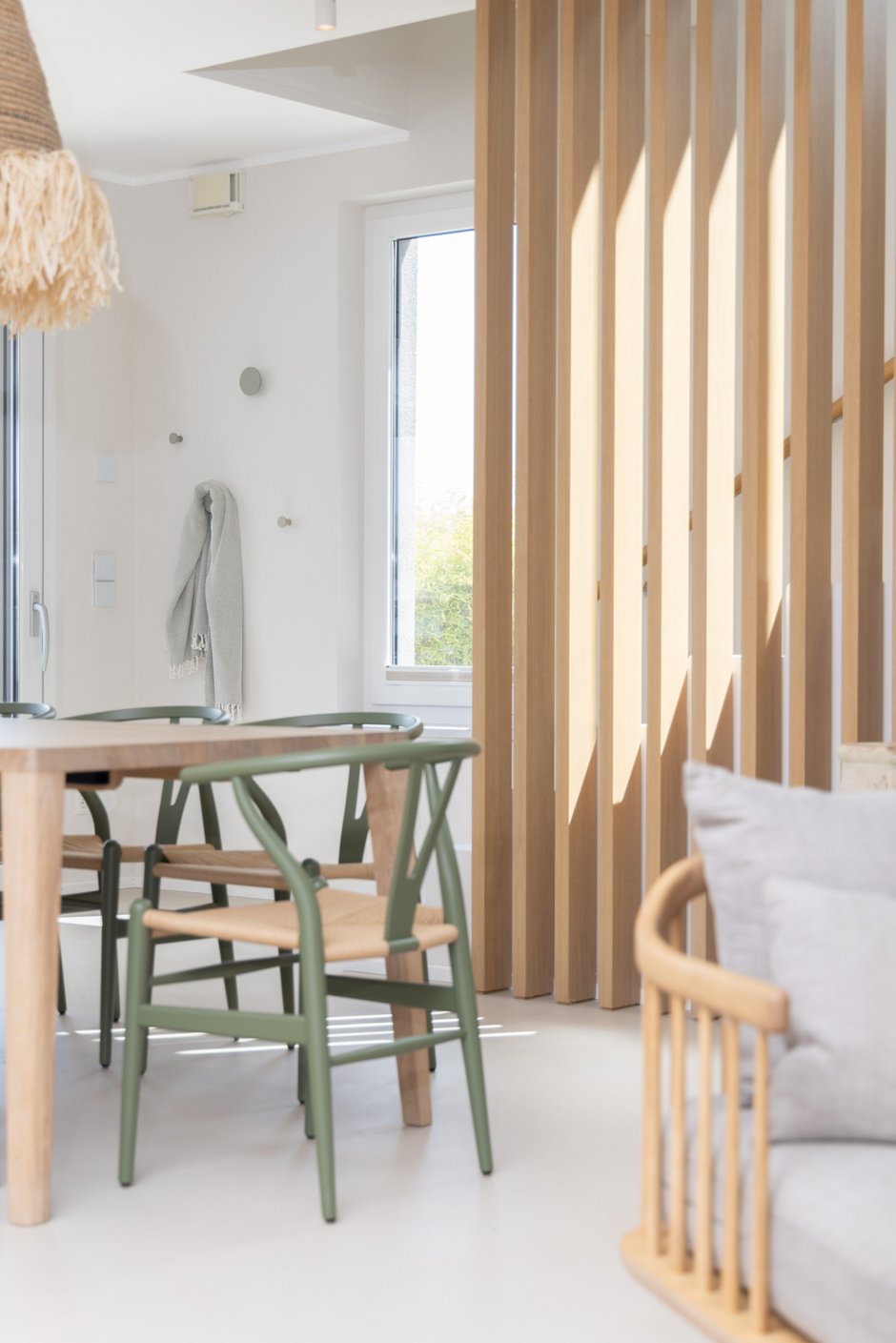 Haus am See im Burgenland: Holzlamellen mit Sonnenstreifen, Esstisch mit grünen Stühlen und Decke am Wandhaken