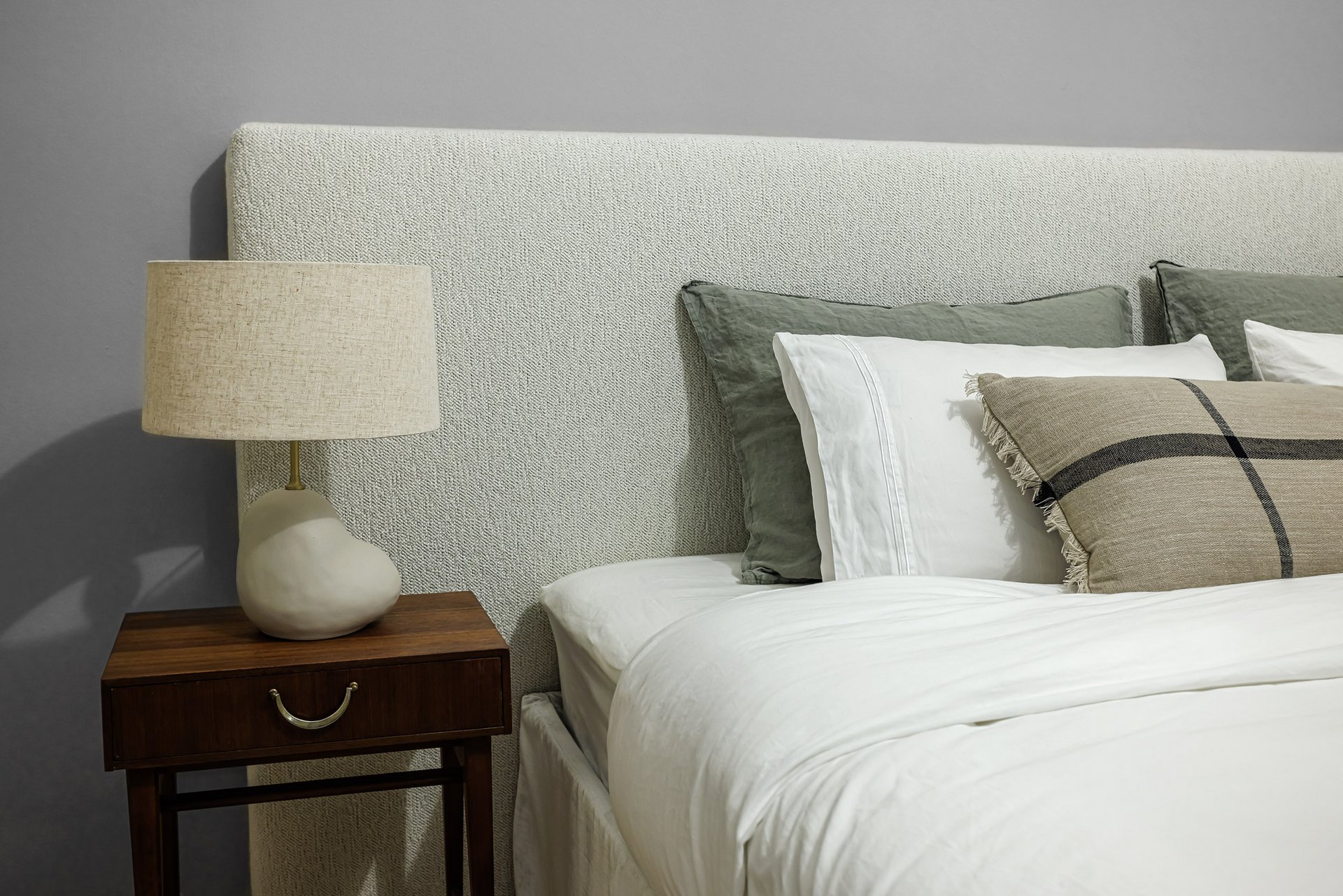 Interiorfotografie – Details, Materialien und Gestaltung im Schlafzimmer Detailaufnahme eines Schlafzimmers mit gepolstertem Kopfteil, Nachttisch, Lampe und abgestimmten Textilien.