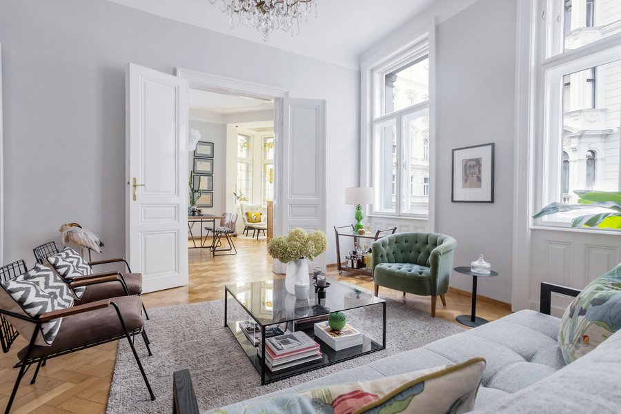 Altbauwohnung in Wien – Interiorfotografie Helles Altbau-Wohnzimmer in Wien mit Fischgrätparkett, grünem Samtsessel, Glastisch und offenen Flügeltüren